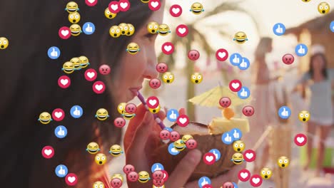 múltiples iconos digitales flotando contra la mujer caucásica bebiendo cóctel de coco en la playa