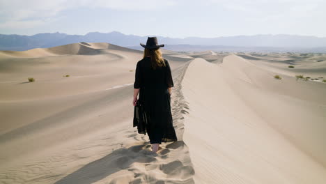 mujer vestida de negro caminando sobre una duna de arena en el parque nacional del valle de la muerte en california, ee.uu. - tiro de seguimiento