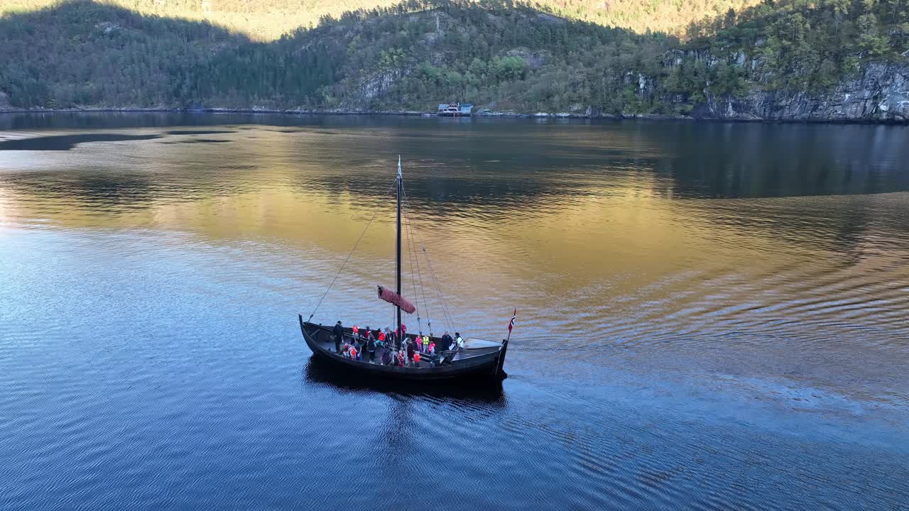 Slow motion drone shot of children and adults on a traditional wooden ship in Veafjord, wearing lifejackets and exploring the fjord