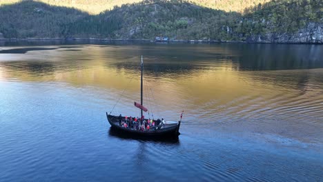 slow motion drone shot of children and adults on a traditional wooden ship in veafjord, wearing lifejackets and exploring the fjord