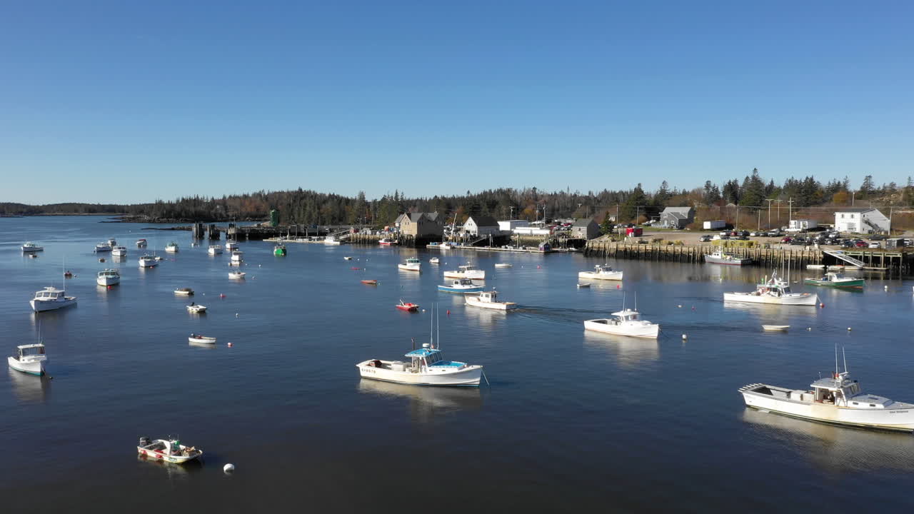 Dronekuva ylilennolta veneestä, joka lähtee satamasta pysäköityjen veneiden ympäröimänä, Mainen rannikolla, Vinalhavenissa, Foxsaarilla, Knox Countyssa, Mainessa, USA.
