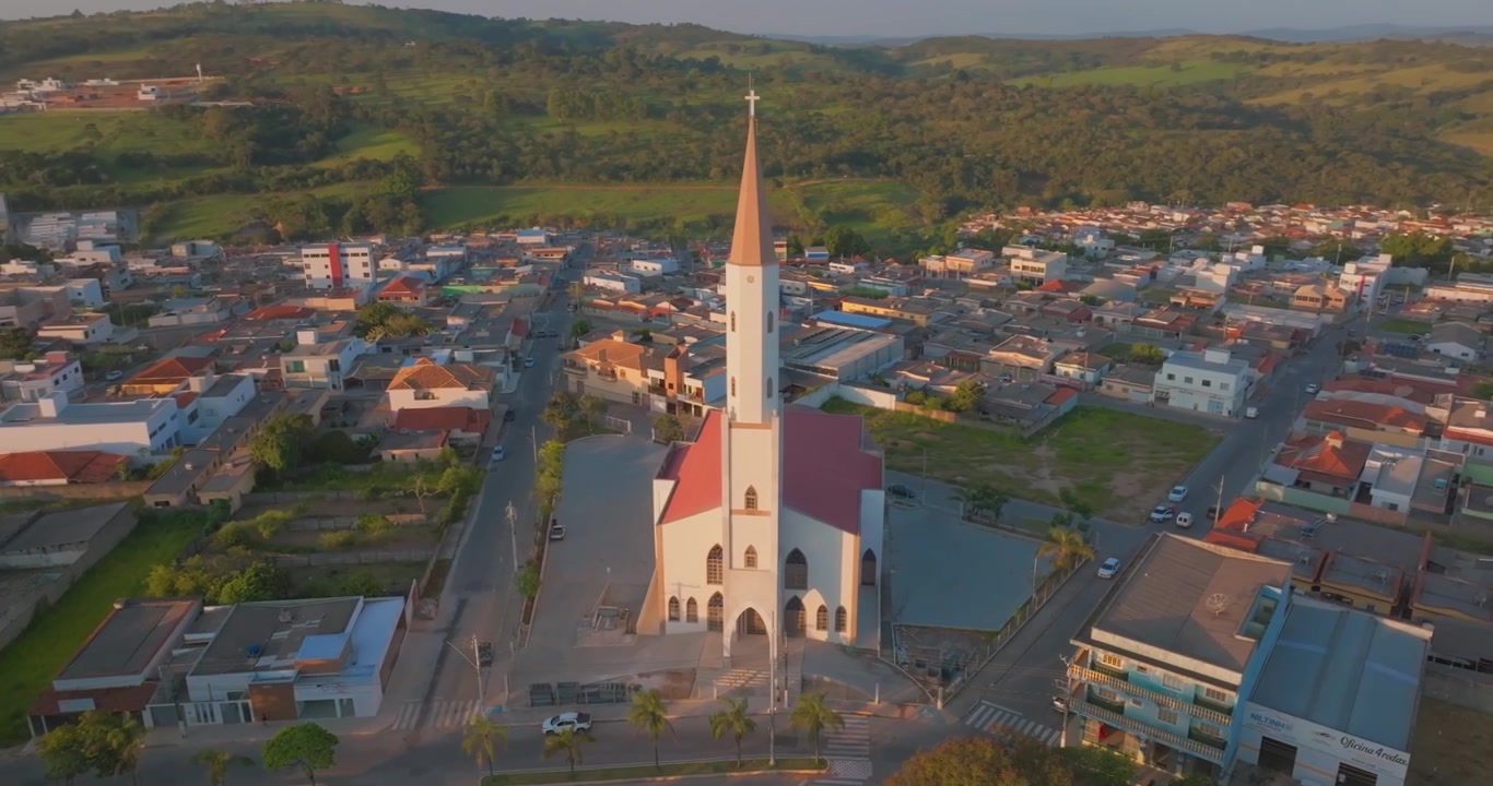 Die Antoniuskirche erhebt sich über der Innenstadt von Santo Antônio do Monte, Minas Gerais, Brasilien, den Wohnvierteln und sanften grünen Hügeln im Abendlicht, Drohnen-Orbit-Einstellungsaufnahme im Uhrzeigersinn.
