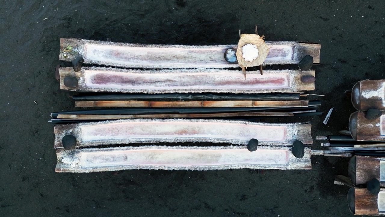 Saline tradizionali con sale bianco appena raccolto conservato in cesti di legno, che mostrano la produzione artigianale di sale e i processi naturali di evaporazione solare, riprese aeree in allontanamento.
