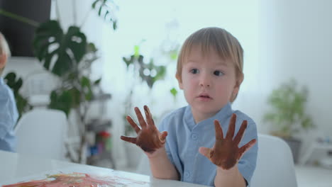 the boy leaves handprints on paper with the help of a jerk. drawing fingers with pomuschiyu paints. development of creative skills in children