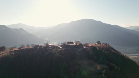 El-Sol-Del-Amanecer-En-La-Cordillera-Brilla-Sobre-Las-Ruinas-Del-Castillo-De-Takeda,-El-Paisaje-Japonés-En-Hyogo-Asago,-Disparo-Aéreo-De-Drones