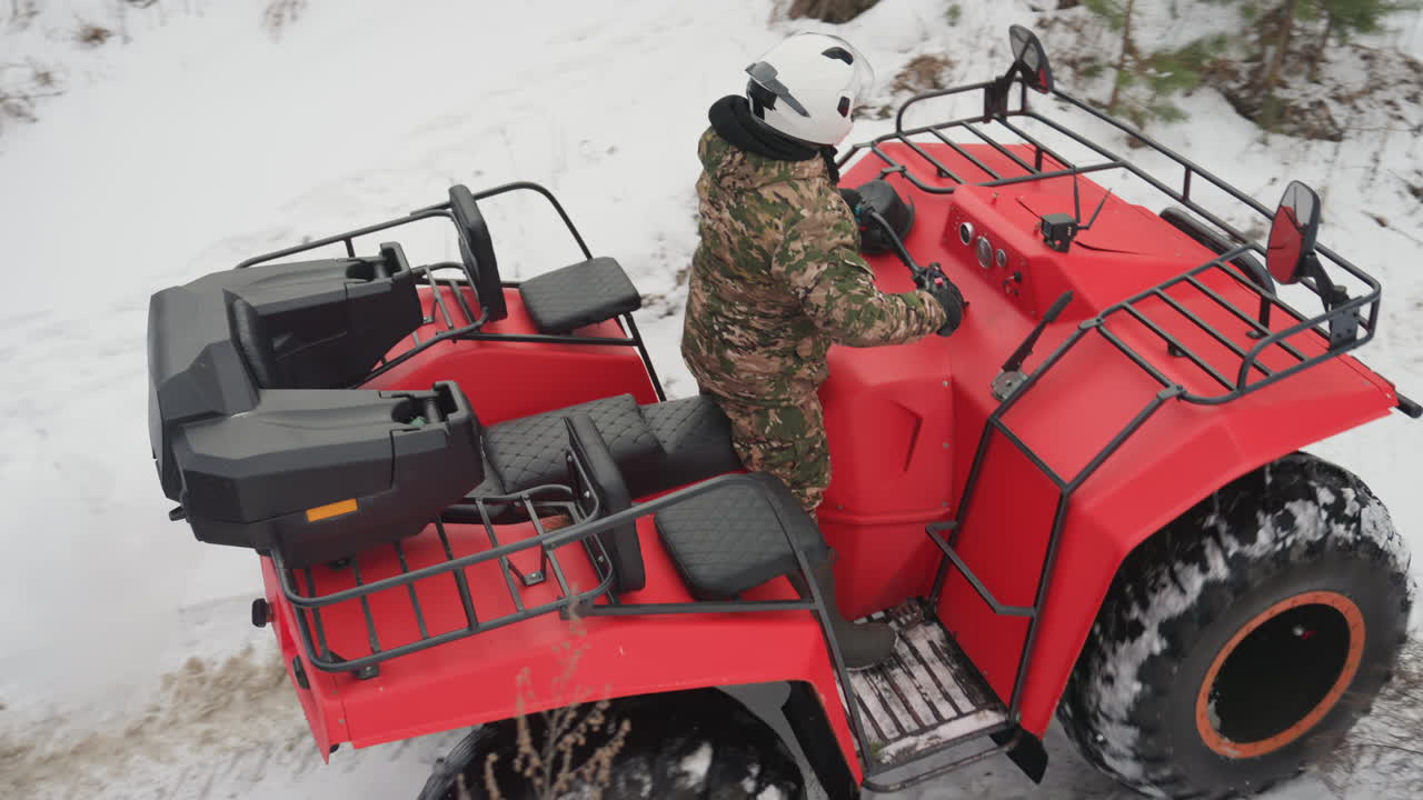 ATV rosso che scala una collina innevata, il pilota sale un ripido pendio con acceleratore e controllo della trazione. Gli pneumatici affondano nel gelo e nella neve soffice, segni di derapata e spruzzi creano una dinamica scena fuoristrada.