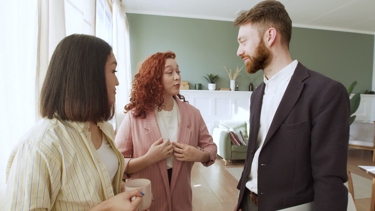 Three Multiethnic Friends Standing In The Living Room And Talking Together 1