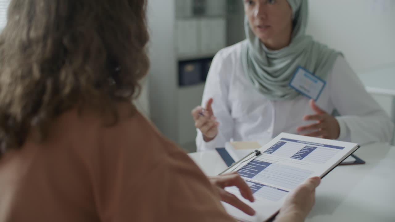 Dokter Wanita Berhijab Menjelaskan Formulir Medis kepada Pasien saat Konsultasi