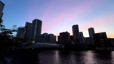 city skyline at dusk with colorful sunset reflecting on a calm river