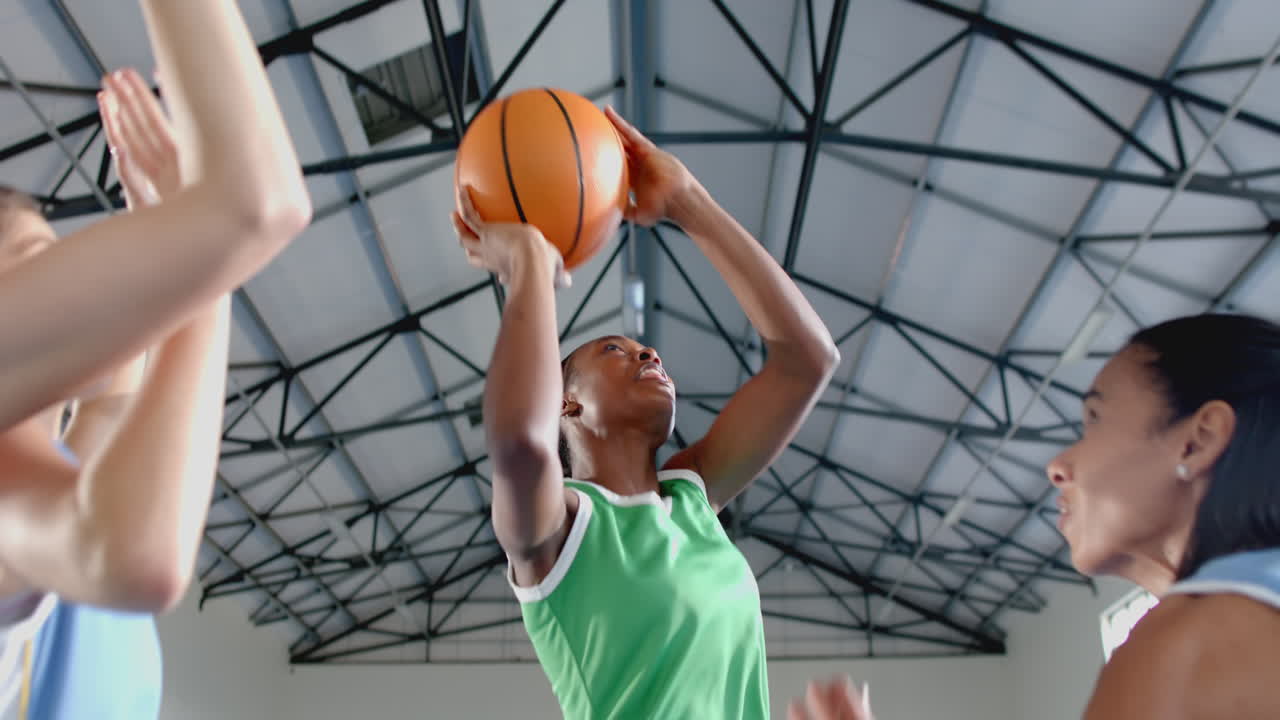 Playing basketball, female athletes reaching for ball during game in indoor court