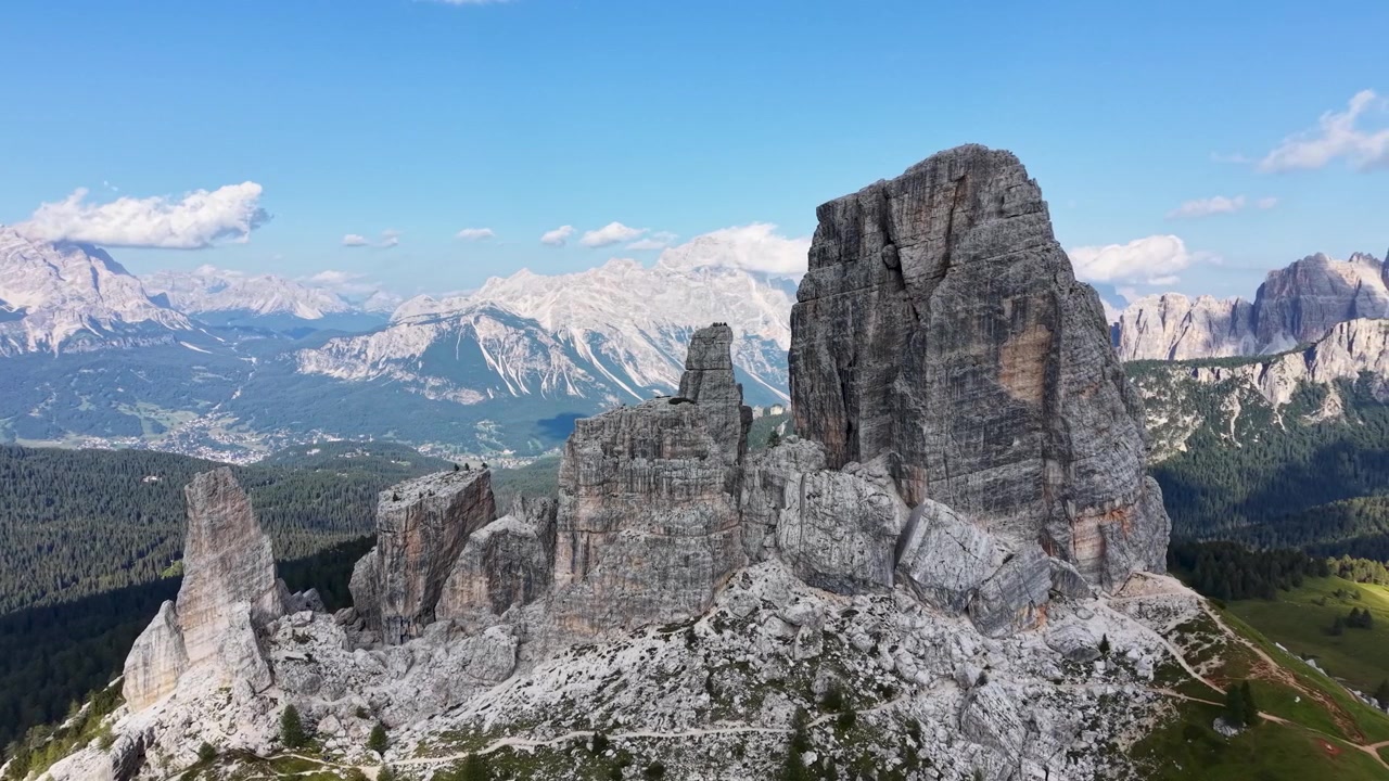 Vista aerea con drone delle formazioni calcaree delle Cinque Torri vicino al Passo Giau, circondate da ghiaioni scoscesi, pendii boscosi e vaste cime dolomitiche
