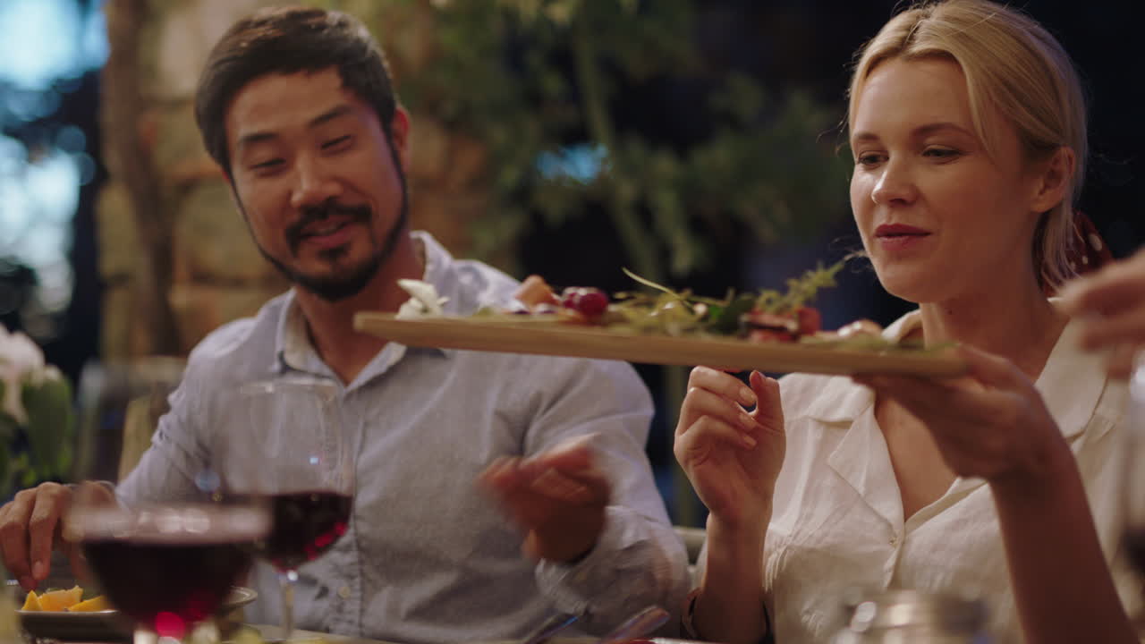 행복한 친구들이 저녁 파티에서 축하하고 지중해 음식을 먹고 접시를 나누고 테이블에 앉아 저녁 식사를 즐기고 있습니다. 4k 영상