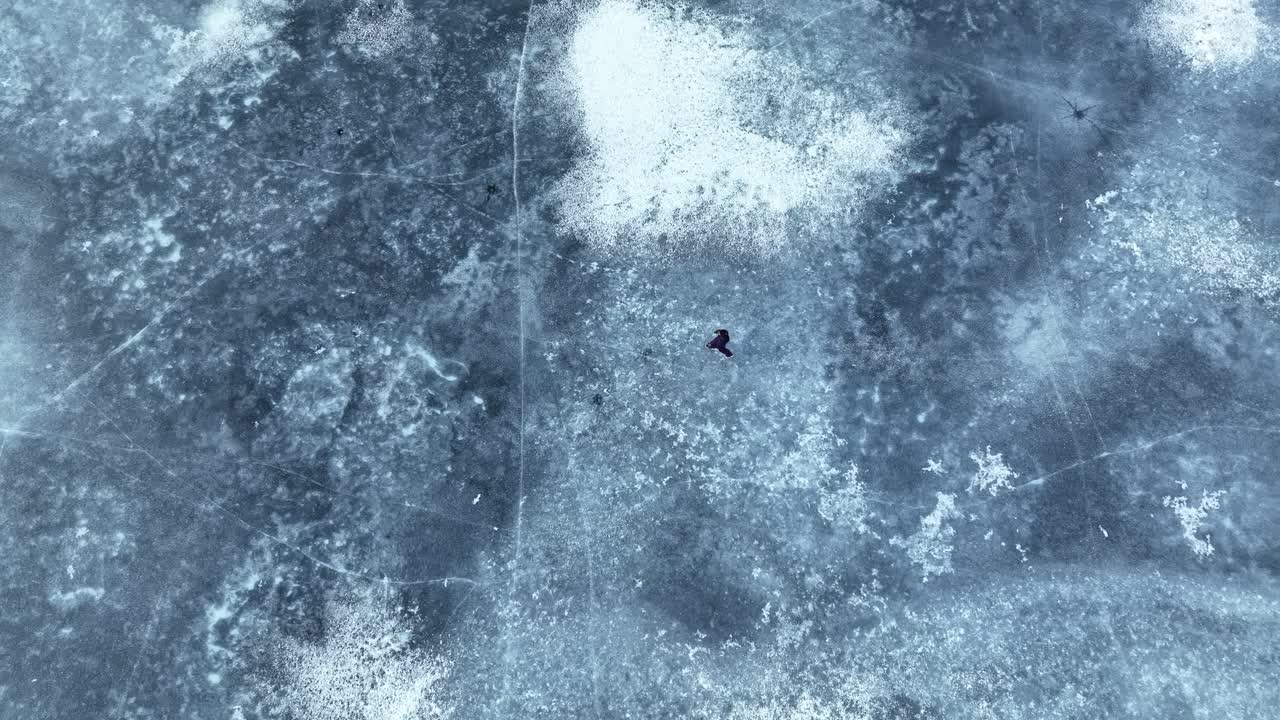 Top Down view follows woman walking steadily across frozen fjord ice in quiet winter conditions in Norway, 60fps