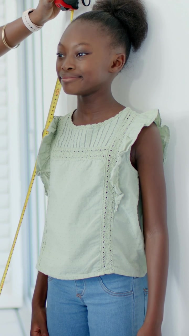 Vertical video: Coming adult measuring height with tape at home, child standing in green top jeans