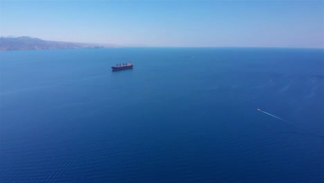 large cargo ship and small boat in vast blue ocean