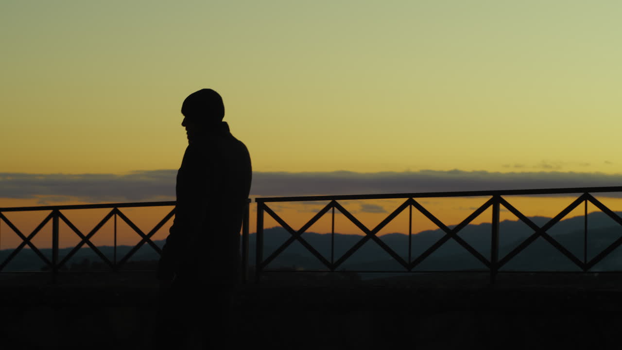 バルコニーで日没時に電話で話している神経質な怒った男のシルエット