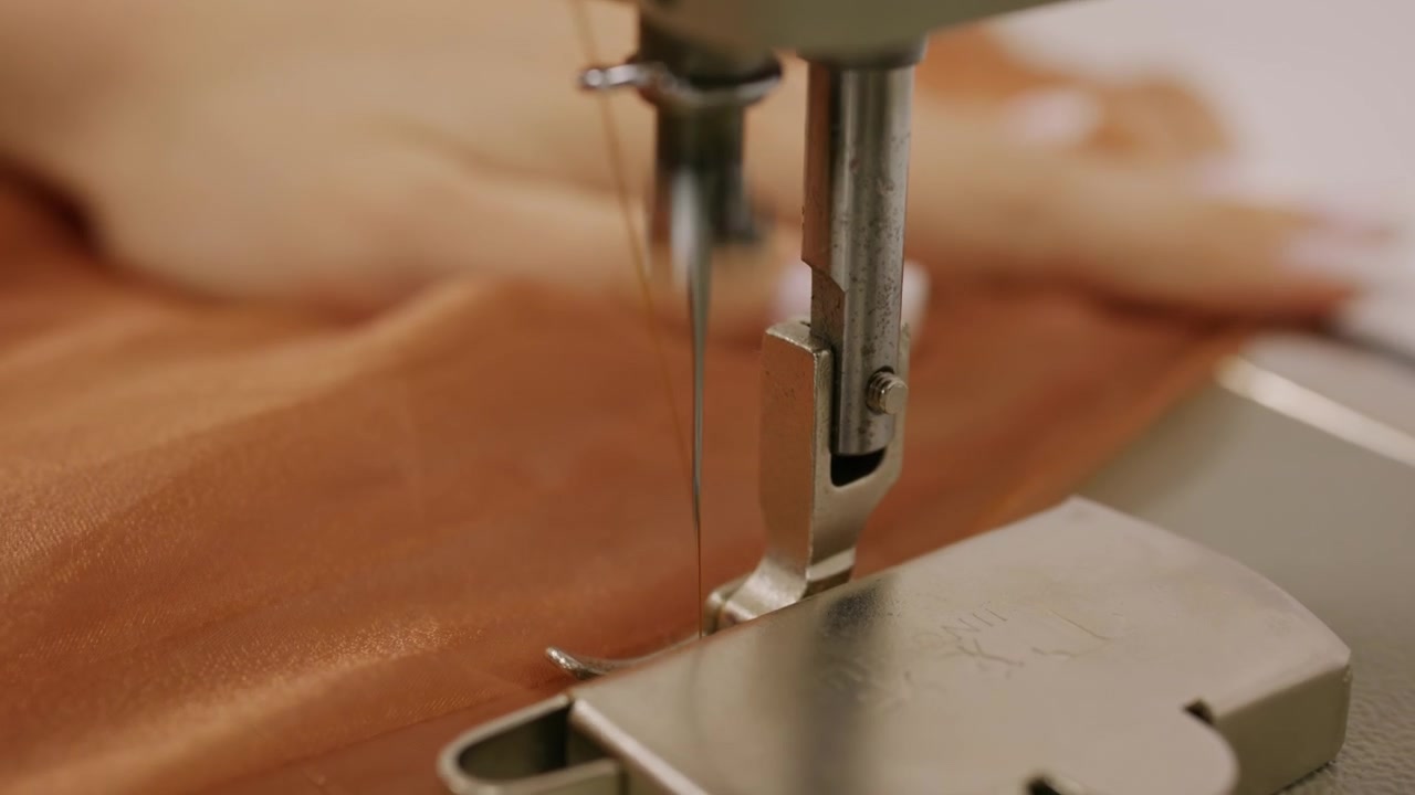 Close up of a person guiding brown sheer fabric under the needle of an industrial sewing machine