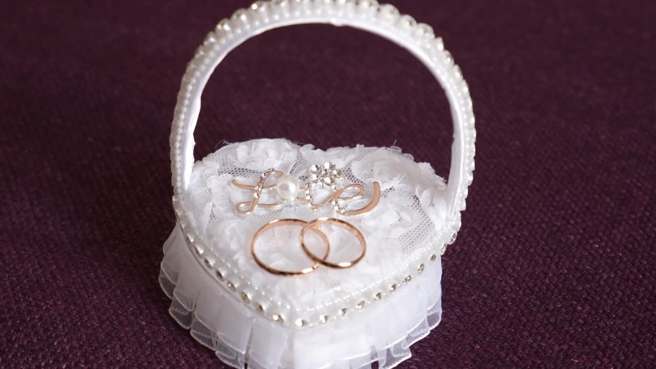 Close up of golden wedding rings on a white lace basket with pearl details