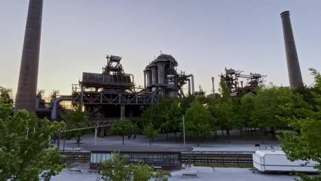 drone-recording-of-the-landscape-park-in-duisburg-germany-in-the-evening-over-the-historical-site,-with-blast-furnace,-metal-struts-and-chimney