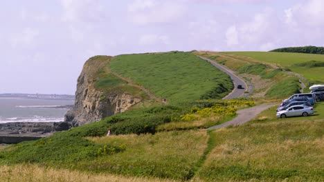 camera pan from natural landscape car park revealing beautiful welsh beach dunraven bay with vehicle driving up hillside with waves breaking in the ocean 4k