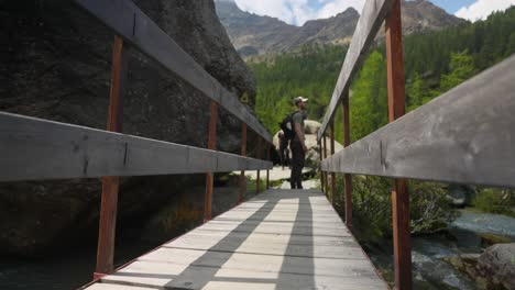 Caminante-Con-Mochila-Caminando-Por-El-Puente-De-Madera-Hacia-El-Alpe-Ventina-En-Valmalenco,-Sondrio,-Italia