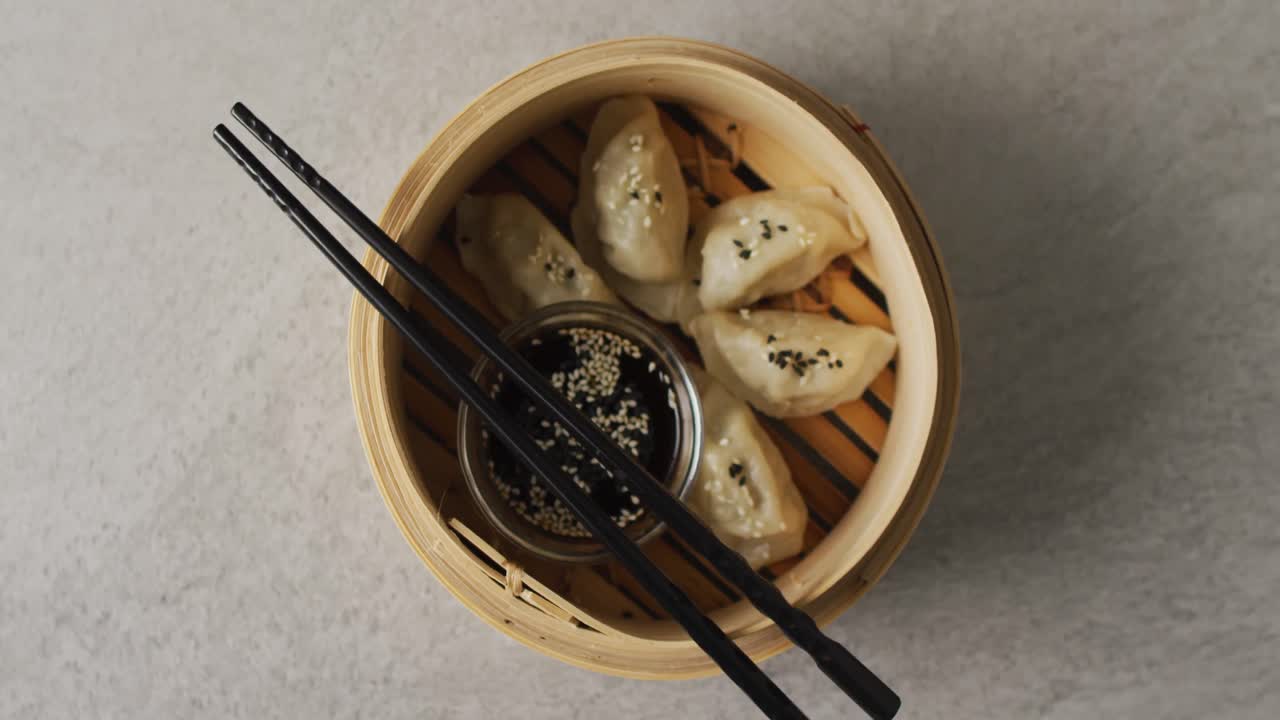 Composition of bamboo steamer with gyoza dumplings and chopsticks with soy sauce on grey background