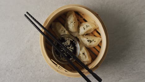 composition of bamboo steamer with gyoza dumplings and chopsticks with soy sauce on grey background