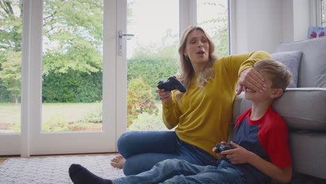 mother and son at home playing video game together with woman cheating to win