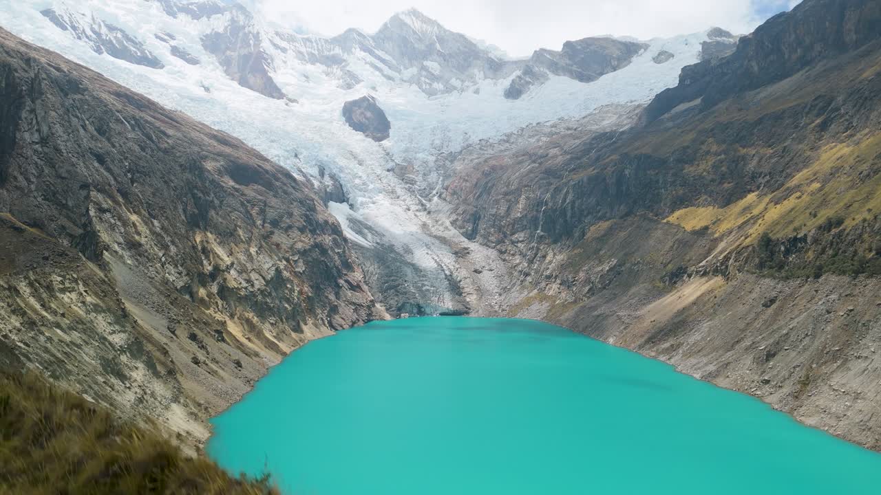 Drone shot rising above highland vegetation to uncover vivid glacier lake and towering snowy mountains in the Peruvian Andes