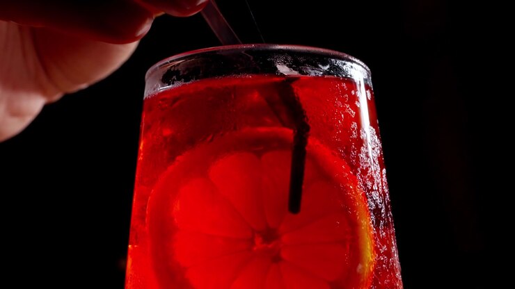 Primo piano macro di un cocktail rosso con guarnizione di agrumi posizionato con pinzette da chef, condensa ghiacciata