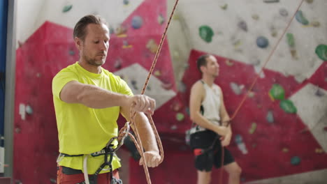 man belaying another climber on an indoor climbing wall. a man using insurance climbers holds the rope and insures his partner who climbs the mountain