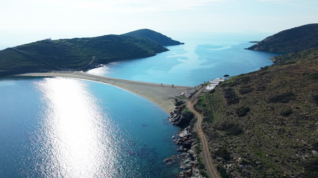 Coastal aerial overview of Kythnos island at golden hour with rugged terrain and calm water reflections, approach to Kolona Beach