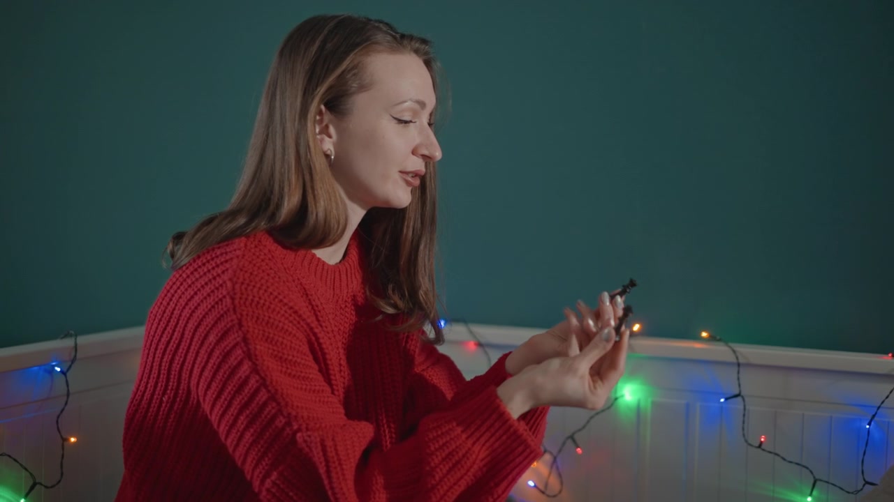 Una figlia adolescente e il padre di mezza età sono seduti sul letto accanto a lucine calde, mentre si scambiano un piccolo regalo incartato. Lei lo tiene con entrambe le mani e lui si protende in avanti, condividendo un momento di celebrazione accogliente.
