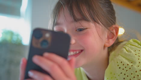 Chica-Sonriente-En-El-Dormitorio-Acostada-En-La-Cama-Usando-El-Teléfono-Móvil