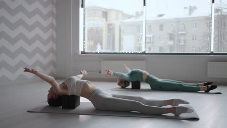 two slender young women perform back exercises lying on cubed platforms. stretching and tone of the back muscles. improvement of posture