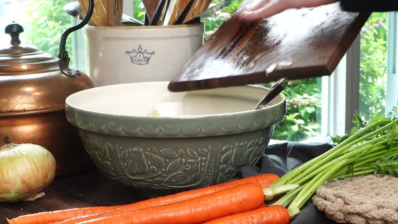 Making meatballs for Italian Wedding Soup. Adding yellow diced onions or shallots into a big green ceramic bowl on a counter in the kitchen. Fresh vegetables like carrots and onions on the counter.