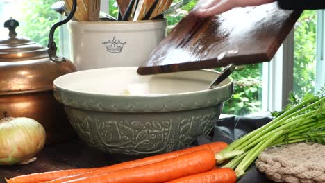 making meatballs for italian wedding soup. adding yellow diced onions or shallots into a big green ceramic bowl on a counter in the kitchen. fresh vegetables like carrots and onions on the counter.