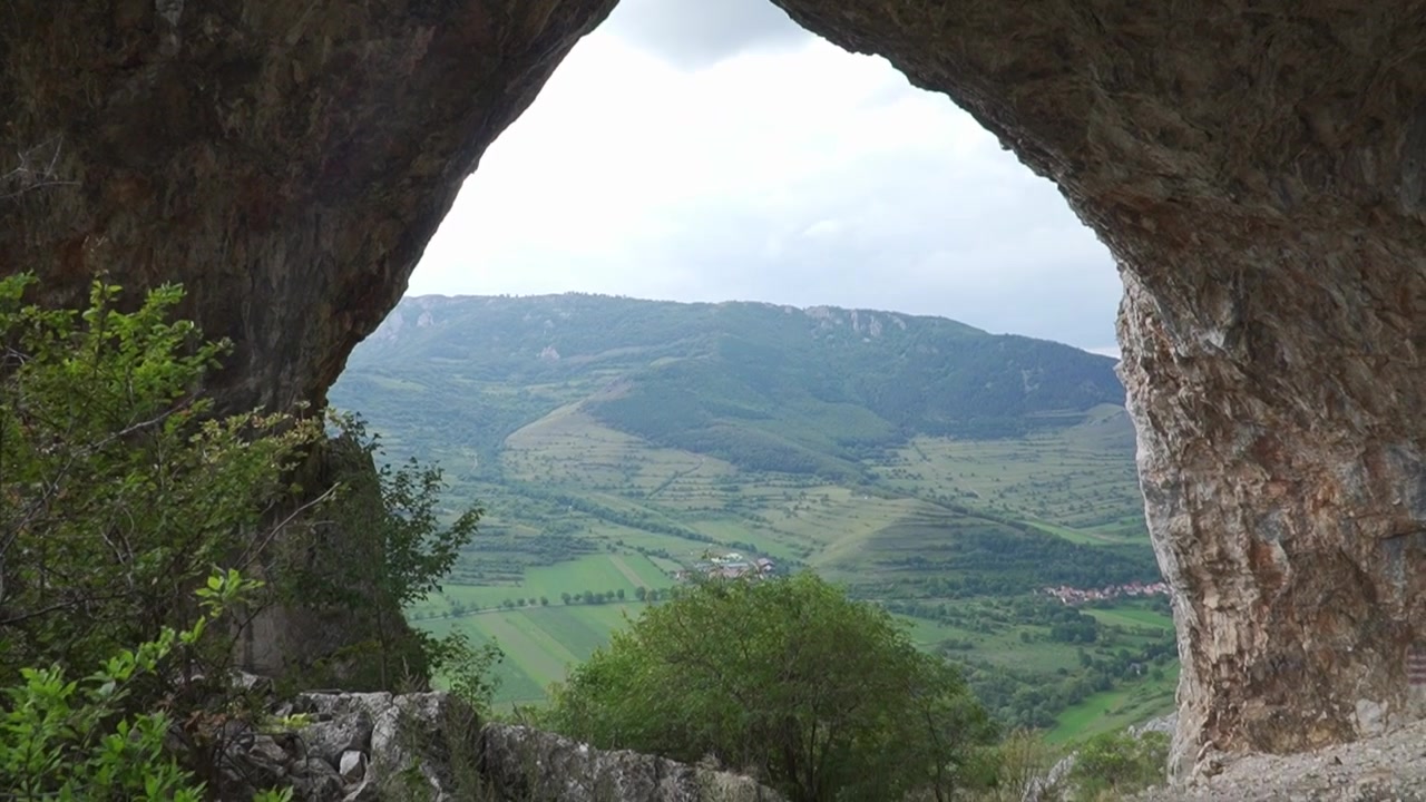 Una vista mozzafiato attraverso un arco di roccia naturale si apre su un vasto paesaggio di montagne e valli.