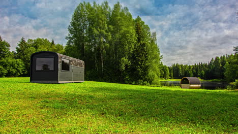 Static-shot-of-sun-rising-in-timelapse-over-regangular-cabin-beside-a-barrel-sauna-in-a-secluded-area-at-daytime