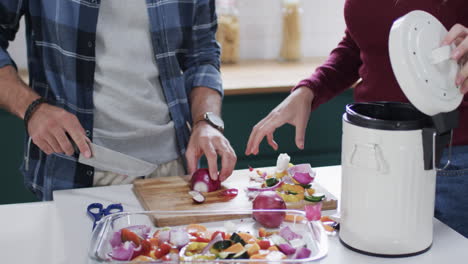 midsection of diverse couple cleaning vegetable peelings in kitchen, slow motion