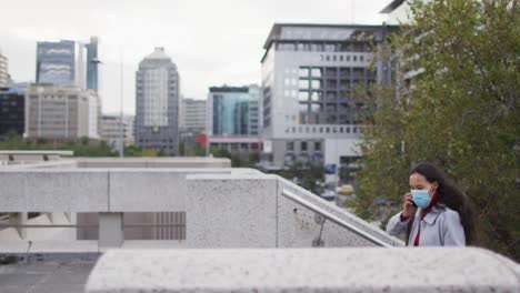 Asian-woman-wearing-face-mask-walking-up-the-stairs-and-talking-on-smartphone