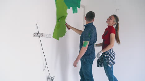 man in shirt paints wall with green near happy wife in room