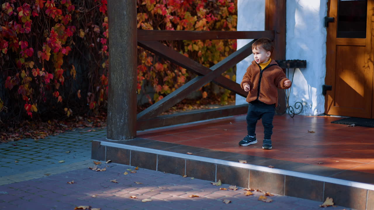 Little kid steps on the porch. Cute child happily hopping from the stair in autumn outdoors.