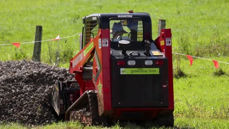 a mini skid steer loader operates on a farm, moving gravel with precision under bright daylight conditions
