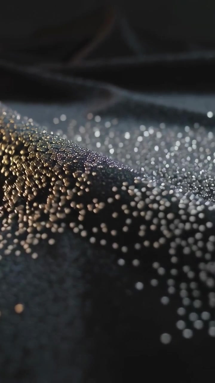 Vertical video: Shifting shiny beads reacting to moving colored light in studio, forming line