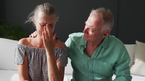 Portrait-of-caucasian-senior-woman-crying-while-her-husband-supporting-her-at-home