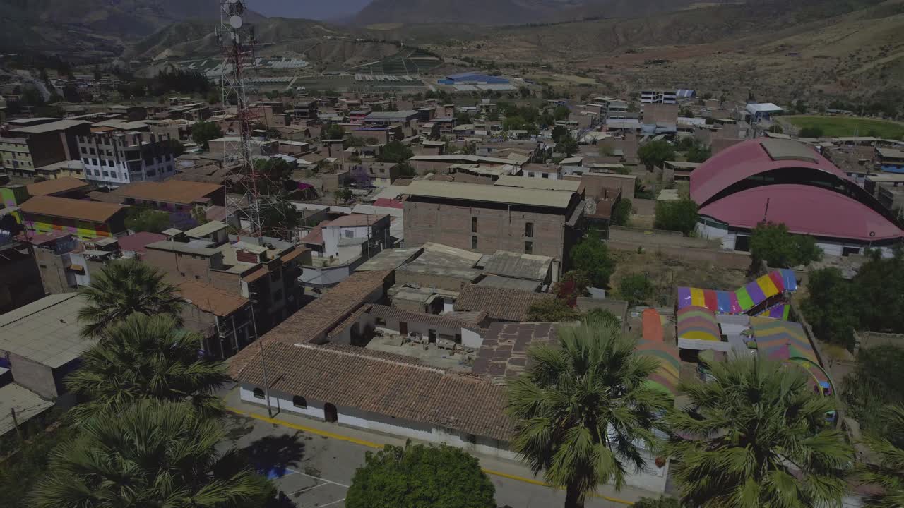 Veduta aerea di una piazza cittadina con campanili e montagne.