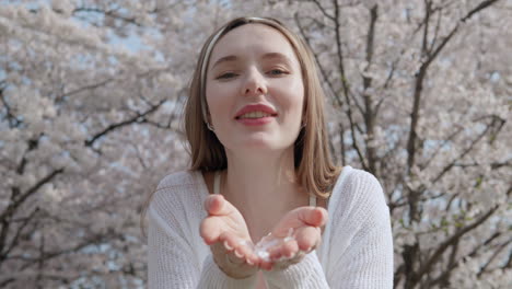 caucasian woman blowing cherry blossom petals in her hands