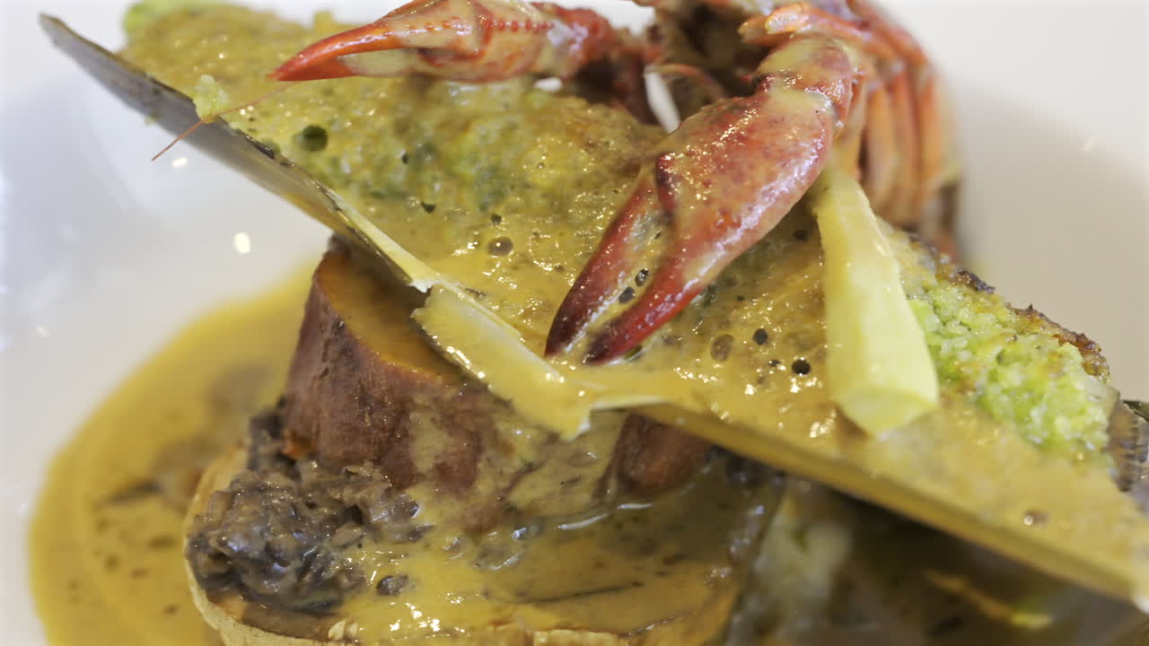 Close up of whole cooked crayfish with a mussel shell filled and a creamy herb topping on a white plate
