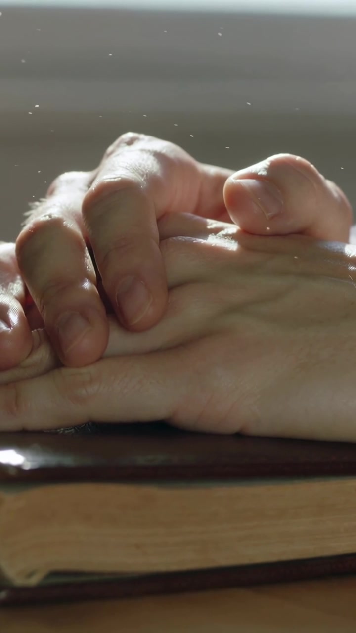 Vertical video: Resting two hands adjusting on closed book by window, daylight showing dust motes